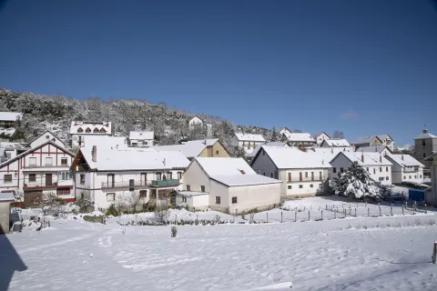 Casas tradicionales pirenaicas con fachadas blancas y tejados nevados en Abaurrea Alta, montes al fondo.