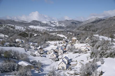 Pueblo de Abaurrea Baja en invierno con iglesia, casas de piedra blanca y montañas nevadas del Pirineo de fondo.