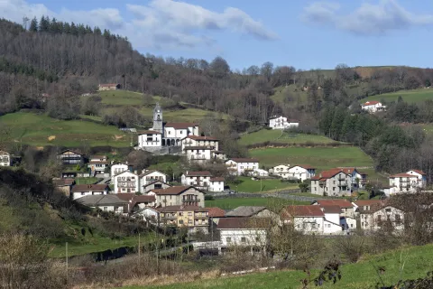 Pueblo de Areso con iglesia de campanario blanco rodeado de casas dispersas entre prados y bosques.
