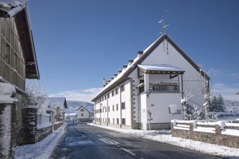 Señalización de entrada a Auritz-Burguete con escudos heráldicos cubiertos de nieve y paisaje pirenaico nevado de fondo.