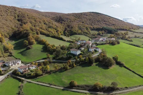 Valle verde con pueblos dispersos entre montes boscosos en Basaburua, rodeado de prados y vegetación de otoño.