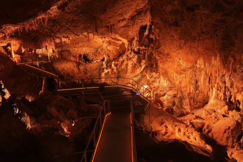 Cuevas de Mendukilo por dentro, con estalactitas y estalacmitas alumbradas con luces anaranjadas.