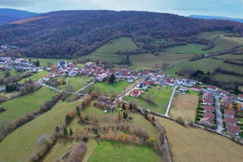 Vista aérea de Espinal en otoño tardío, pueblo pirenaico navarro rodeado de prados verdes y arquitectura tradicional de tejados rojos.