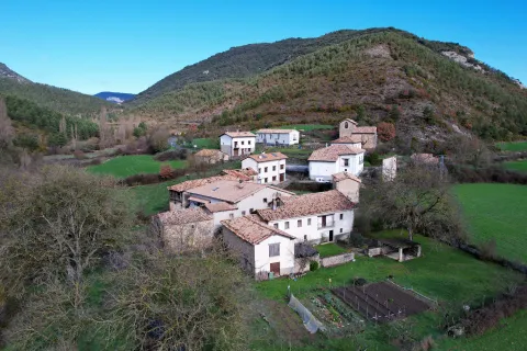 Valle de Gallues con casas de piedra tradicionales, prados verdes y montañas boscosas al fondo.