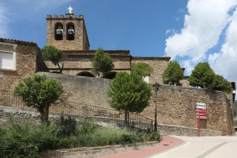 Iglesia rural de Liédena con torre campanario de piedra, arcos románicos y vegetación.