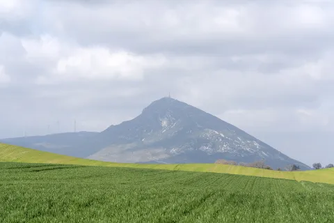 Prado verde delante de la Higa de Monreal, que tiene a su lado molinos de viento.