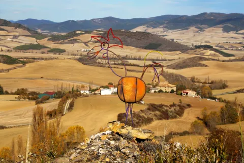 Escultura de metal colorida sobre roca con vista panorámica al valle agrícola desde la Peña Izaga.
