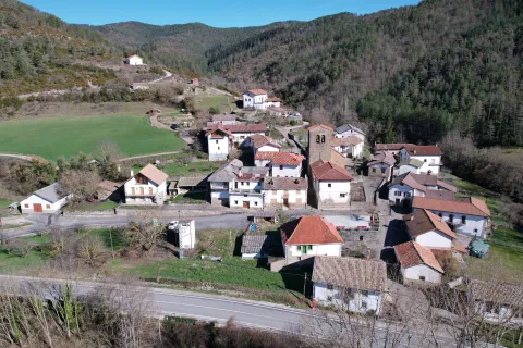 Vista aerea del pueblo de Sarries con casas de piedra y tejados rojos rodeadas de bosque y prados verdes en el Pirineo de Navarra.