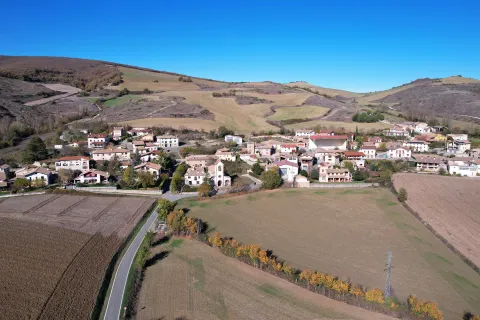 Pueblo de Unciti del prepirineo con campos de cultivo y montañas al fondo bajo cielo despejado.