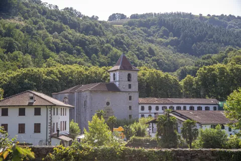 Vista panorámica del pueblo de Urdax inmerso en vegetación verde, con iglesia visible y montes boscosos.