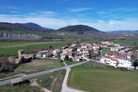 Pueblo de Urraul Bajo visto desde el aire con castillo medieval, caseríos dispersos y campos verdes.