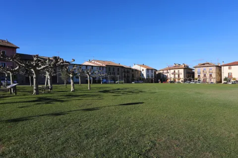Jardin verde de Urroz-Villa con casas de piedra al fondo y árboles bajo cielo despejado.
