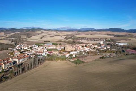 Vista aérea de Urroz-Villa con casas, campos de cultivo y montes al fondo.