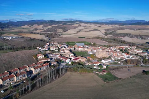 Vista aérea de Urroz-Villa con casas, campos de cultivo y montes al fondo.