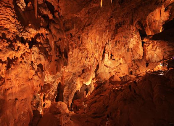 Cuevas de Mendukilo por dentro, con estalactitas y estalacmitas alumbradas con luces anaranjadas.