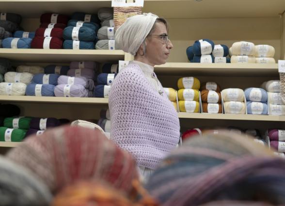 Mujer en tienda de lanas en El Gantxillo de Mari, rodeada de estanterías con ovillo de colores variados.