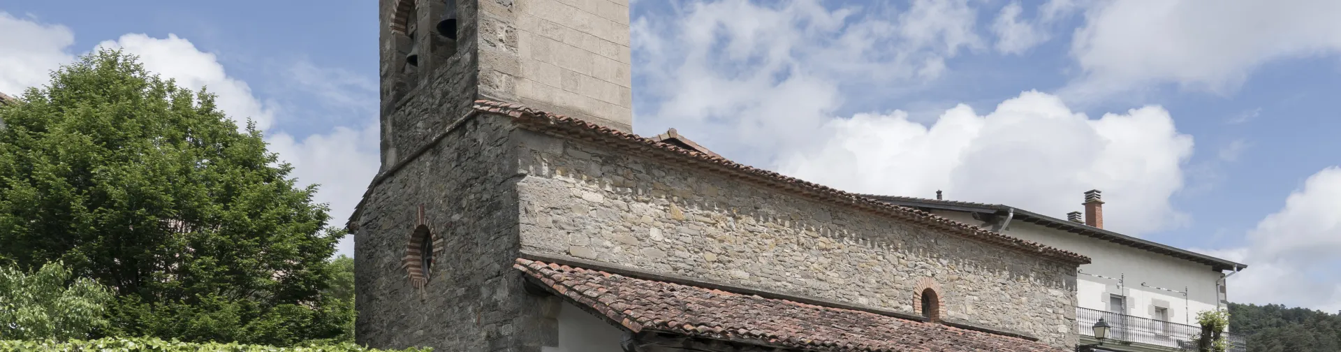 Iglesia parroquial romanica de piedra con torre campanario en Agorreta, Pirineo navarro, rodeada de vegetacion.