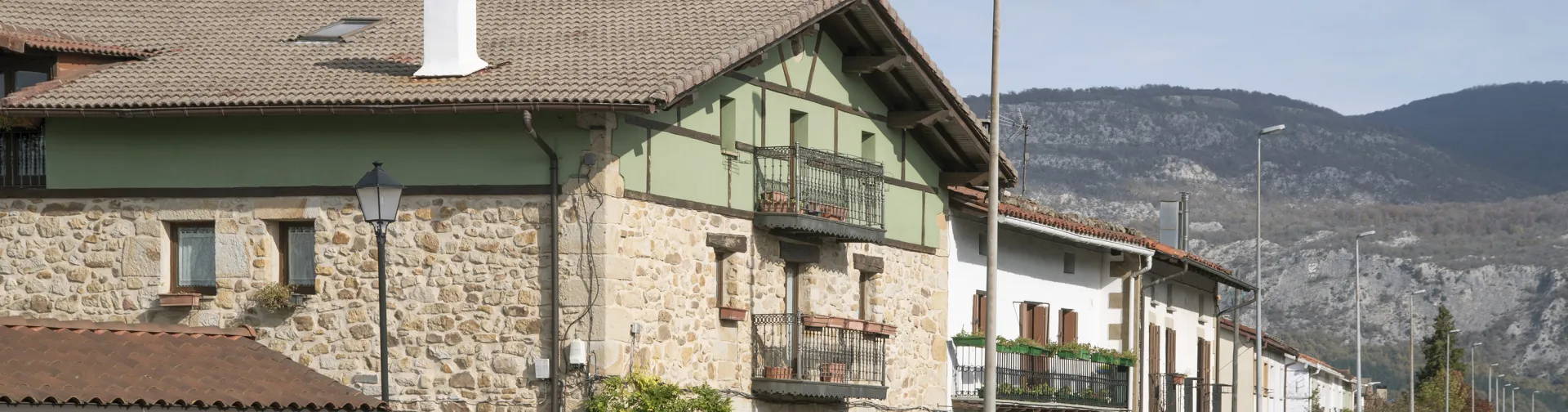 Calle principal de Arbizu con casas de piedra, balconadas y montañas al fondo bajo cielo nublado.