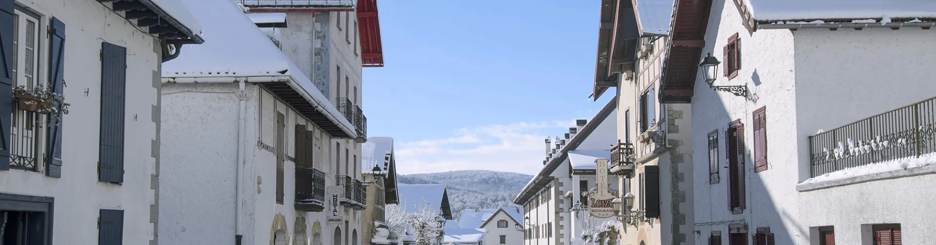 Calle invernal de Auritz-Burguete con edificio principal blanco de arquitectura pirenaica y nieve en Navarra.
