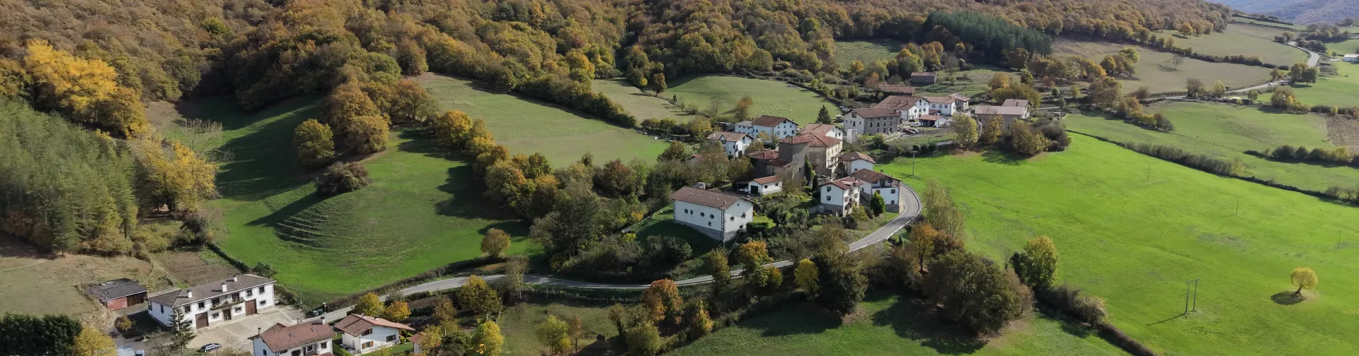 Valle verde con pueblos dispersos entre montes boscosos en Basaburua, rodeado de prados y vegetación de otoño.