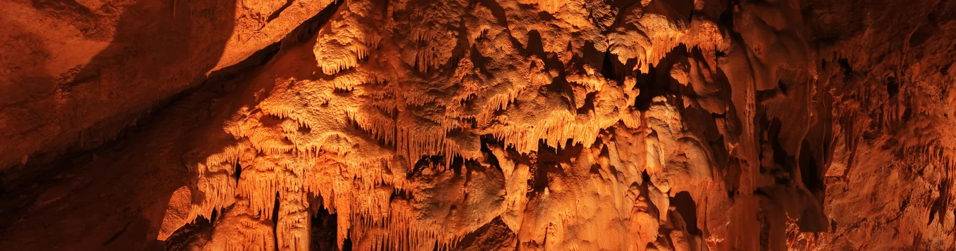 Cuevas de Mendukilo por dentro, con estalactitas y estalacmitas alumbradas con luces anaranjadas.