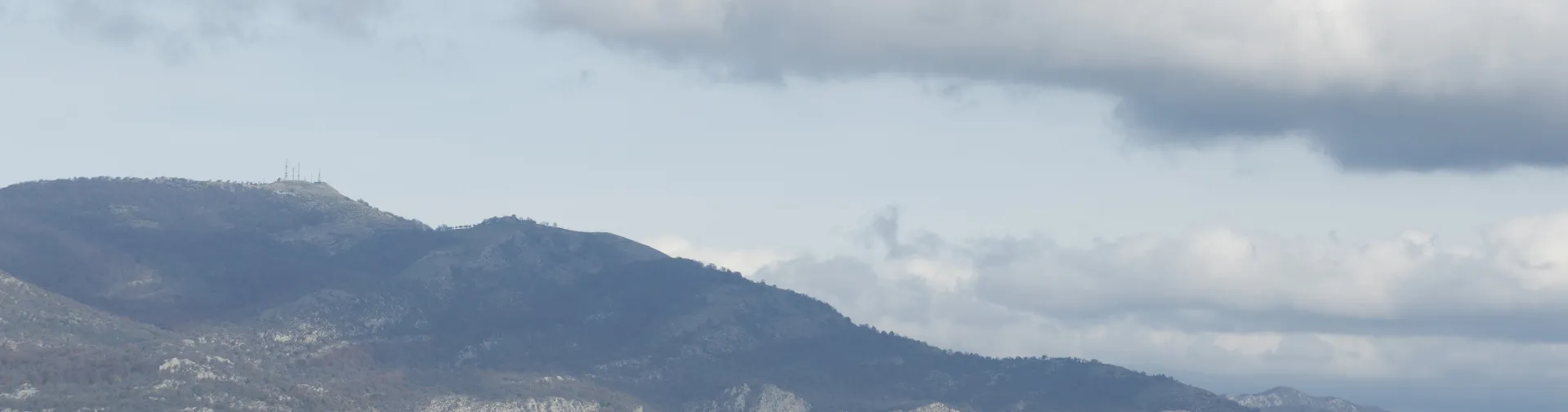 Etxarri Aranaz al pie de la sierra, con montañas al fondo y cielo nuboso en la composición panorámica.
