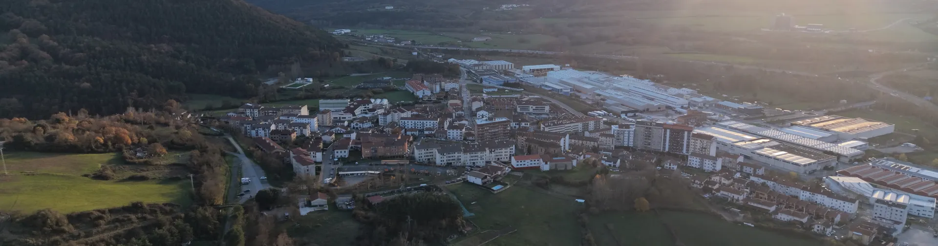 Vista aérea de Irurtzun con montañas al fondo, pueblo rodeado de bosques y prados.