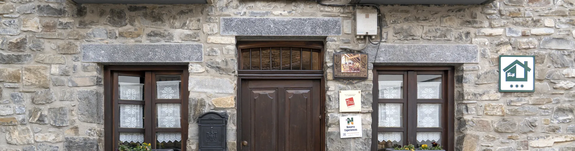Fachada de piedra de casa rural Katalingarde en Isaba, Pirineo de Navarra, con balconadas de hierro forjado y puerta de madera.