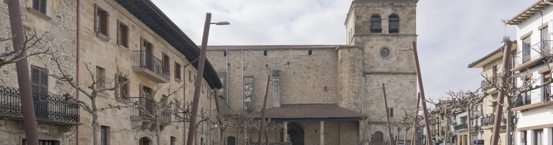 Plaza de Lakuntza con iglesia de piedra, casas tradicionales y árboles desnudos.