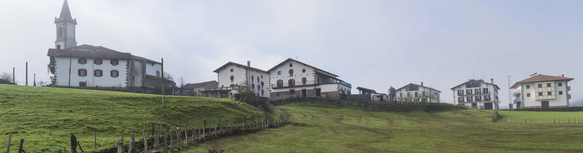 Panorámica de Lekaroz con iglesia, casas dispersas y prados verdes.