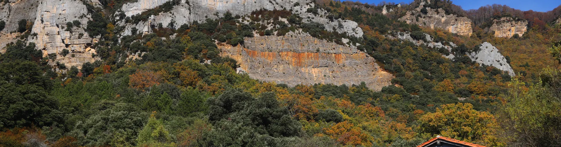 Acantilados calizos de Sierra de Leyre con prado verde y cabaña con mural histórico en primer plano.