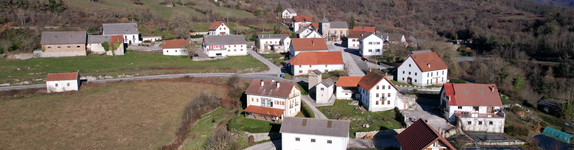 Vista aérea del pueblo de Orbara con casas de piedra y tejados rojos rodeadas de prados verdes y montañas boscosas.