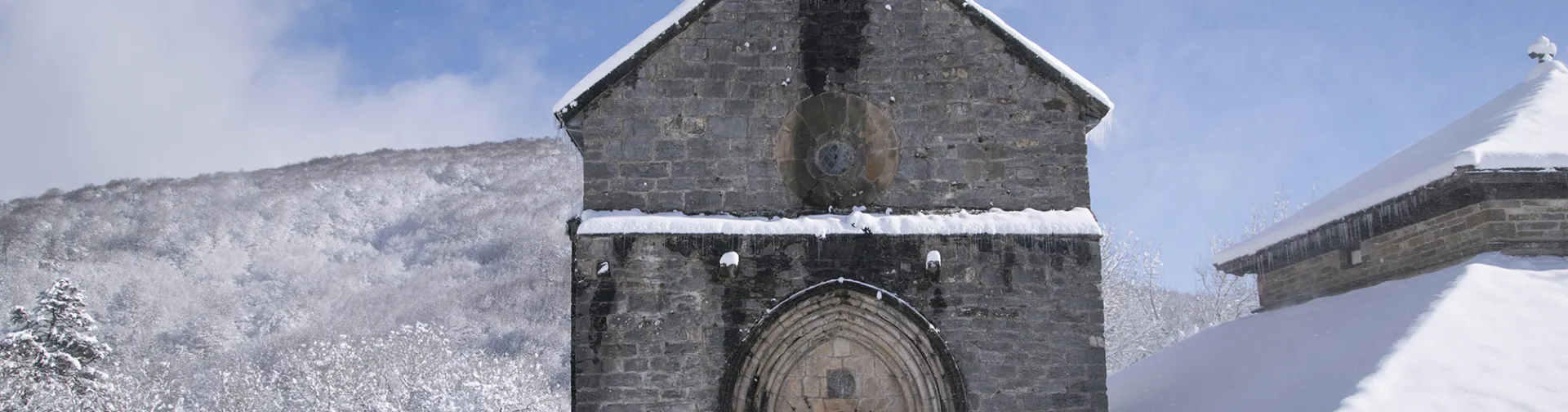 Capilla de piedra medieval con campanario en Orreaga rodeada de nieve y montañas nevadas de fondo.