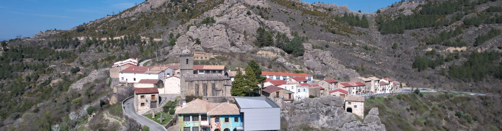 Petilla de Aragón vista aérea con iglesia y casas entre acantilados rocosos y bosque de pinos.