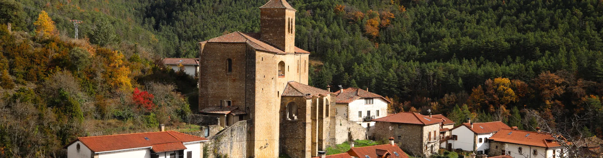 Pueblo de Roncal con iglesia, casas de piedra y tejados rojos rodeadas de bosque pirenaico en otoño.