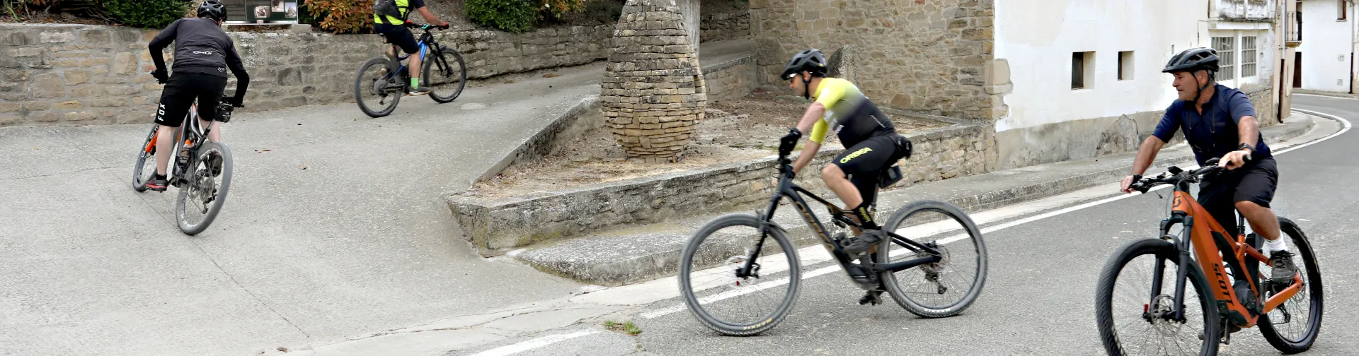 Grupo de ciclistas en ruta por las calles de piedra del territorio Eslava, con arquitectura tradicional al fondo.
