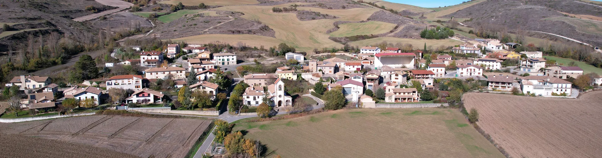 Pueblo de Unciti del prepirineo con campos de cultivo y montañas al fondo bajo cielo despejado.