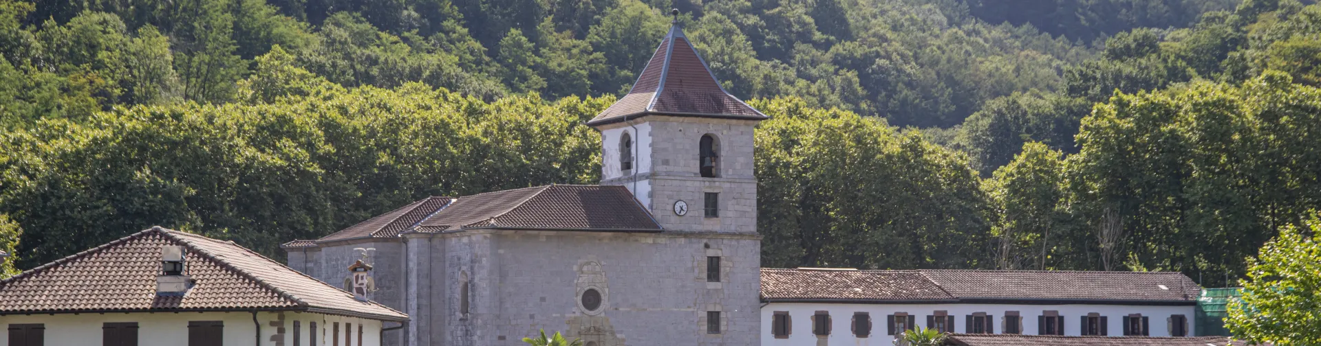 Vista panorámica del pueblo de Urdax inmerso en vegetación verde, con iglesia visible y montes boscosos.