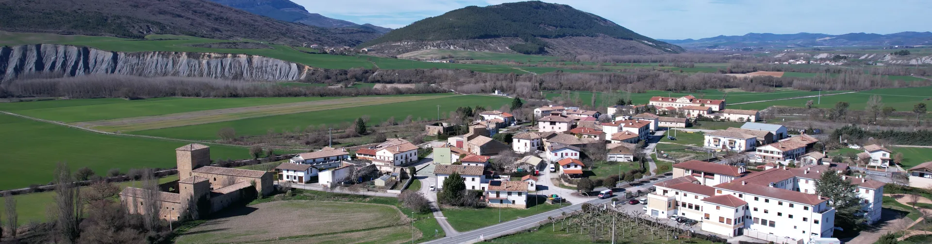 Pueblo de Urraul Bajo visto desde el aire con castillo medieval, caseríos dispersos y campos verdes.
