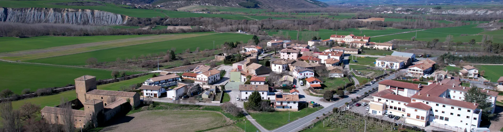 Pueblo de Urraul Bajo visto desde el aire con castillo medieval, caseríos dispersos y campos verdes.