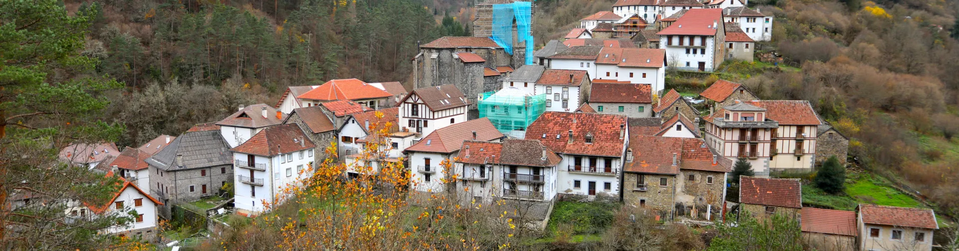 Pueblo de Uztarroz en valle pirenaico con casas tradicionales de tejados rojos, iglesia de piedra y bosques de montaña al fondo en otoño.