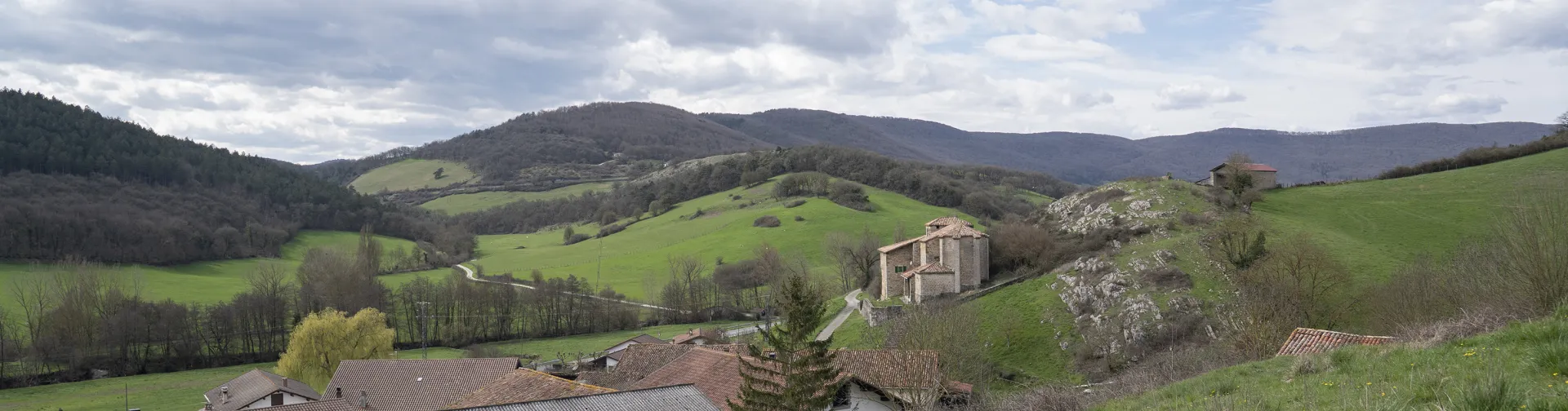 Casas dispersas en el valle de Odieta con iglesia al fondo y montañas verdes.