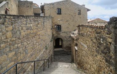 Pasadizo entre muros de piedra con escaleras y barandilla de metal en Aibar, casas de piedra arenisca alrededor.
