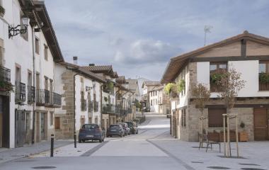 Calle empedrada de Arbizu con casas de piedra blanca y arquitectura tradicional navarra y vehículos aparcados.