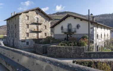 Casas de piedra tradicionales en Areso con balcones y montañas al fondo bajo cielo despejado.