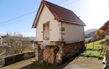 Un horreo, construcción agrícola tradicional, de piedra y con leña debajo en Aria, en paisaje pirenaico de monte verde.