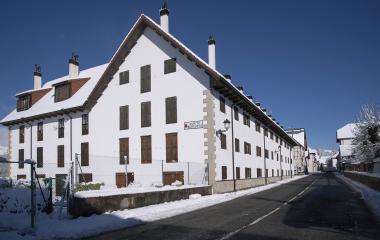 Calle principal de Auritz-Burguete con casas de piedra blanca y montañas nevadas al fondo durante invierno.
