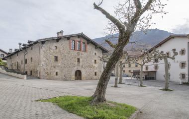 Plaza de Bakaiku con arquitectura tradicional de piedra, árbol y montañas de fondo.
