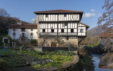 Casa solariega con entramado de madera y piedra en Betelu, junto a río, vegetación y huerta.