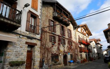 Calle empedrada de Burgui con casas de piedra tradicionales, balconies de madera y flores decorativas en fachadas.